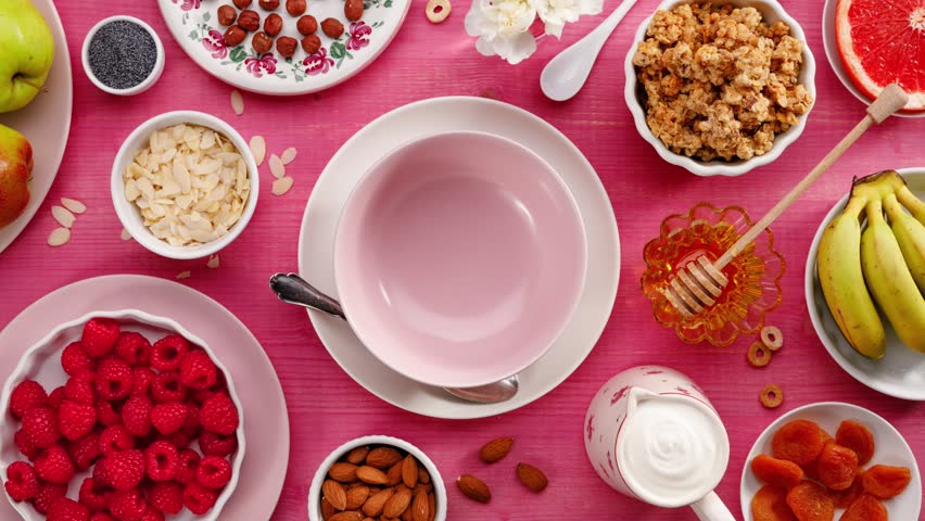Granola with natural yogurt, fresh raspberries, honey, almond flakes and poppy seeds in a ceramic bowl on a pink wooden table, top view. Healthy eating concept, perfect breakfast or dessert. Royalty-Free Stock Footage #1008972806