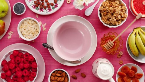 Granola with natural yogurt, fresh raspberries, honey, almond flakes and poppy seeds in a ceramic bowl on a pink wooden table, top view. Healthy eating concept, perfect breakfast or dessert.
