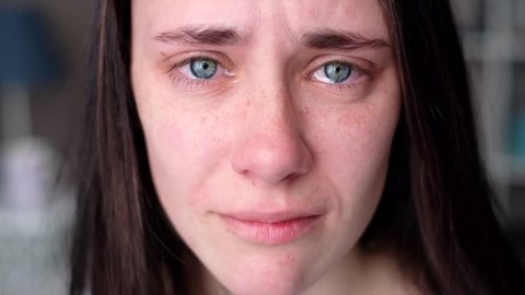 Young woman crying looking at the camera in slow motion. Tears comes out of an eyes