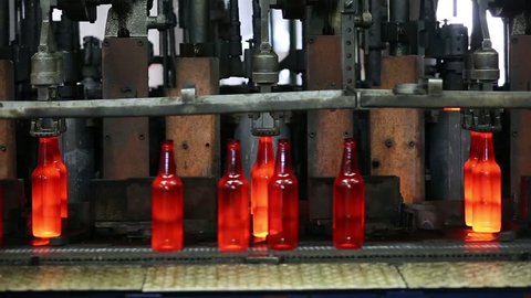 Beer bottle production. Glowing bottles after melting glass on a factory conveyor line with a dark background wide view. Automated Production Line of Bottle In Glass Factory.