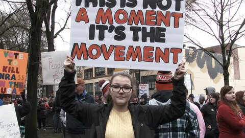 PORTLAND, OREGON / USA - MARCH 24, 2018: Teenage girl joins crowd at March For Our Lives protest against gun violence holding sign, "This is not a moment, it's the movement."