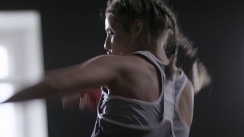 Side view shot of sporty young woman exercising with punching bag and kicking it during boxing workout at the gym, medium shot