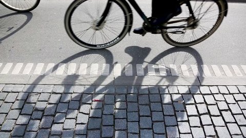 People cycling in Copenhagen, focus on bicycle shadows. Side view of a bicycle lane in the Danish capital, with many persons commuting by bike.
