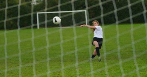 4K Young female soccer player kicking ball into goal, seen from back of the net. Slow motion.