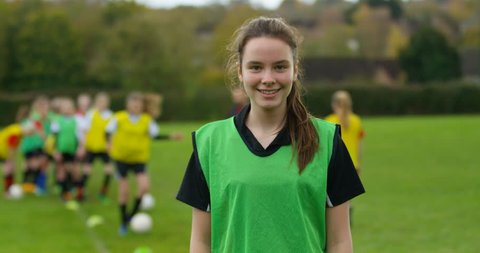 4K Portrait smiling British girl at soccer training, with team mates in the background. Slow motion.
