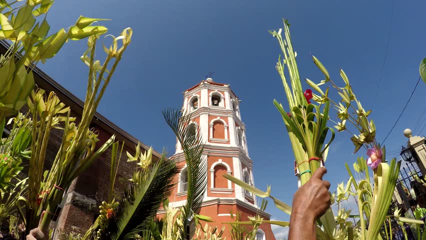 San Pablo City, Laguna, Philippines, March 25, 2018: Church tower background, Catholics waving coconut palm leaves on Palm Sunday. The feast commemorates Jesus' triumphal entry into Jerusalem, Royalty-Free Stock Footage #1009007129