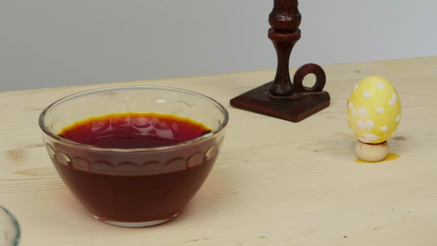 Easter egg after staining on a wooden stand. Next to the egg are glass bowls with paint.