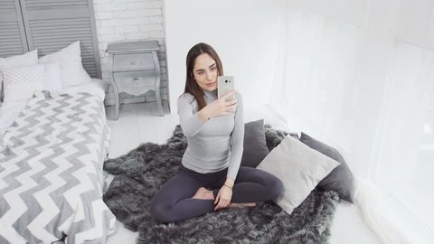 Caucasian female (girl, woman) using phone for self portrait (selfie). White room with window and teddy bear.