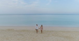 Aerial view of beautiful couple walking on tropical sandy beach over sea and sky background - video in slow motion