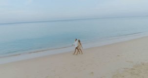 Aerial view of beautiful couple walking on tropical sandy beach over sea and sky background - video in slow motion
