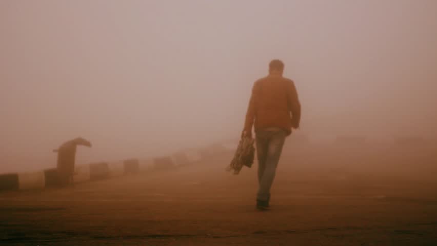 A person walks along the road into the distance. Fog. Desert.