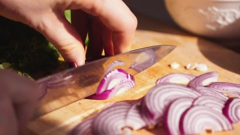 Rapidly Chopping Onion, Close-Up. Slow mothion. red onions close up. Female hands cut onions in kitchen. Macro shooting of red onions. The woman cuts onions on a wooden board.