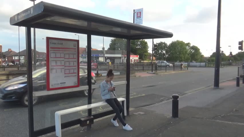 A girl waiting for a bus at the bus stop, and a lot of trees and building as a background, Newcastle upon Tyne, UK