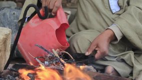 Short video of a hand of a man fill the teapot of water and then put the pot on fire which burns with leaves.