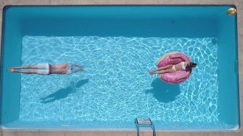 Aerial - Adult man dives into the the pool while girl is lying on a donut pool float