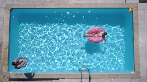 Aerial - Adult man jumps into the the pool like a cannon ball while girl is lying on a donut pool float