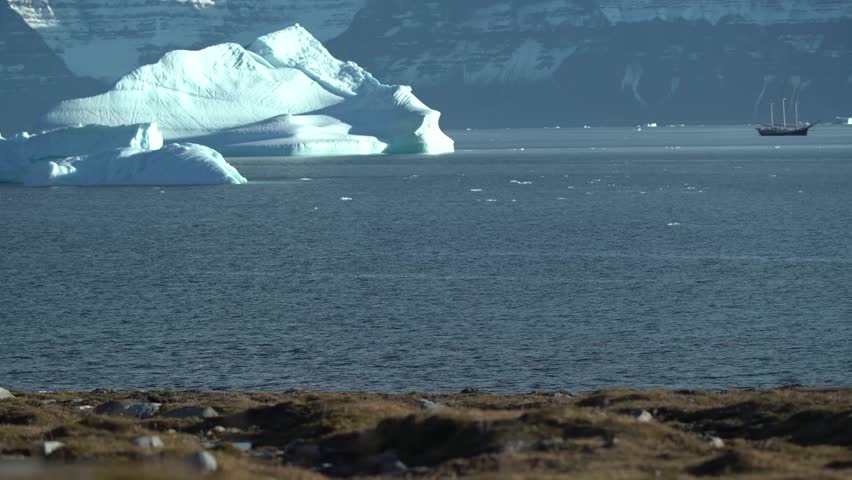 Giant iceberg in a fjord with a tall ship