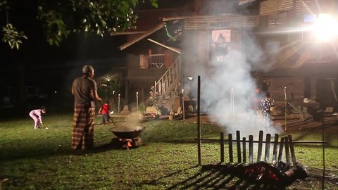 Hari Raya night scenery with man making a famous Malaysian food known as dodol(traditional sweet confection) and kids playing fire cracker during night of Eid ul-Fitr festival celebration.