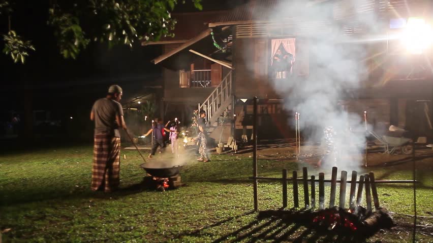 Men making Malaysian traditional food 'lemang' over firewood outdoor kitchen during Eid Mubarak with kids playing firework around vintage village house.Eid ul-Fitr night scene. | Shutterstock HD Video #1009039994