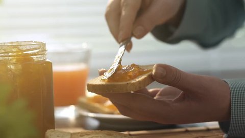 Woman preparing an healthy breakfast at home, she is spreading jam on toasted bread slices, healthy lifestyle concept