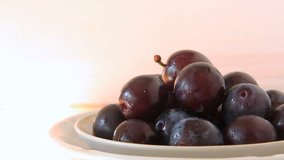 Fresh plums in plate with waterdrops on white background, healthy meal. Plate is turning, close up shot