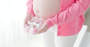 pregnant woman stand and holding small baby shoes