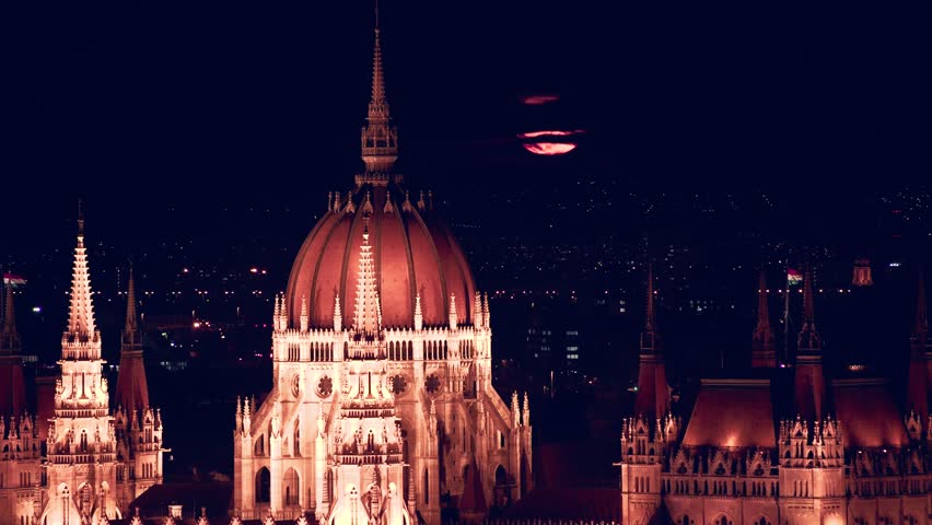 Close up view of a red Super-moon rising behind the Hungarian Parliament Building illuminated at night in Budapest Hungary 