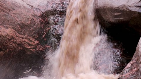 Closeup of little brown waterfall flowing through the rocks