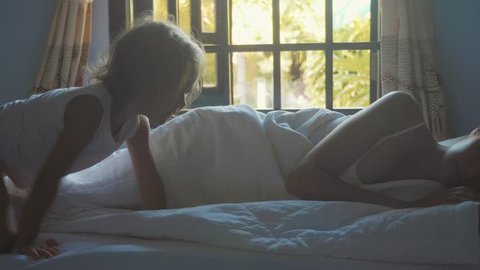 Cute little daughter wakes her mother at morning in slow motion. Little girl crawls on the bed to mother, wakes her and lying near in mom hugs.