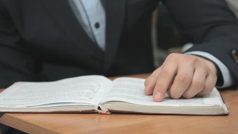 Unknown man dressed in black suit sitting at a table and reading a book. Close-up