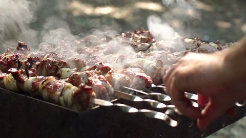 A man's hands rotating the skewers. Shish kebab. Pork or lamb meat pieces being fried on a charcoal grill. Frying grilled pieces of meat during the rest.