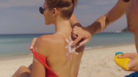Happy couple applying sun tanning lotion on the beach, man putting sunscreen suntan cream on woman - video in slow motion