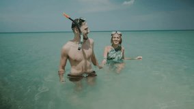 Young happy couple with snorkeling masks having fun in the sea water, enjoying sunny summer day on their beach tropical holiday - video in slow motion