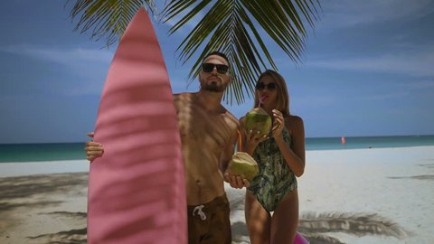 Young happy couple in swimwear drinking coconut milk, enjoying sunny summer day on their beach tropical holiday - video in slow motion