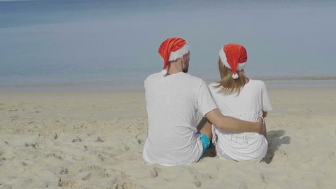 Christmas beautiful beach couple wearing Santa hat in summer sun in love on travel holidays on tropical travel destination during winter holidays - video in slow motion