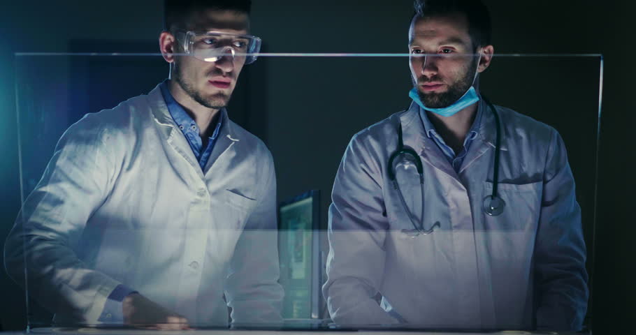 A couple of doctors or scientist analyze the patient's medical situation by checking on a glass monitor with a futuristic holography. Concept of: medicine, doctors, future, holography. Royalty-Free Stock Footage #1009087268