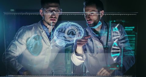 A couple of doctors or scientist analyze the patient's medical situation by checking on a glass monitor with a futuristic holography. Concept of: medicine, doctors, future, holography.
