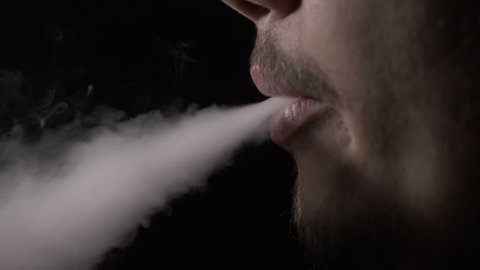 Mouth of a man with beard exhaling smoke from a vaporizer and in the end blowing steam through his nose in slow motion