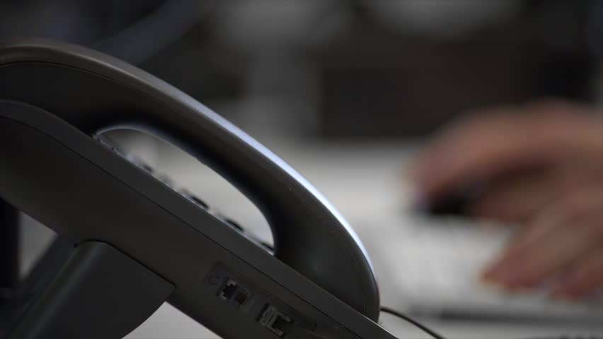 A close-up shot of a male office worker picking up the phone to answer a phone call whilst working at his desk. Royalty-Free Stock Footage #1009097051