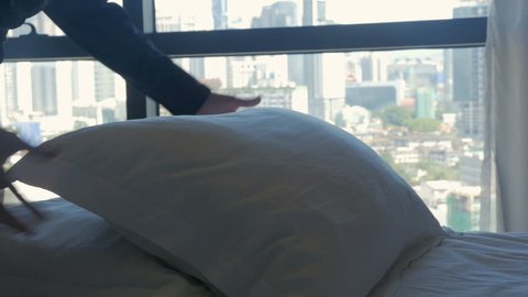 Woman fluffing up pillows on a comfortable bed overlooking a modern city in slow motion