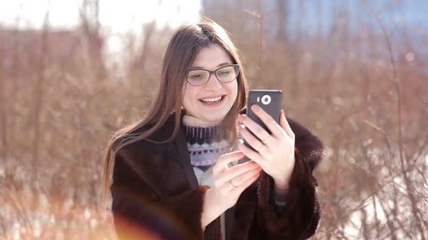 Beautiful girl in a snow-covered winter city using Skype on a smartphone communicates with his family