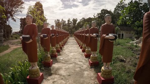 Dozens of identical monk statues with brown robes. standing on pedestals flanking an ancient walkway at Wat Bo temple territory in Siem Reap. Cambodia.