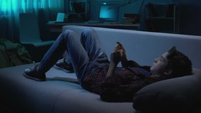 Problem teenager lying on couch and playing game on smartphone at night time