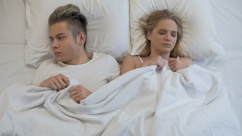Upset young couple lying in bed, angrily pulling blanket, conflict in relations