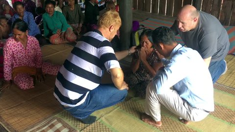 SIEM REAP, CAMBODIA - NOVEMBER 2017: Two Russian Christian missionaries and a Cambodina interpreter pray about a local woman
