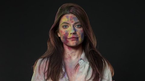Portrait of cheerful woman clapping hands with purple powder and celebrating holi spring festival of colors, isolated over dark gray background slow motion. Indian culture and tradition