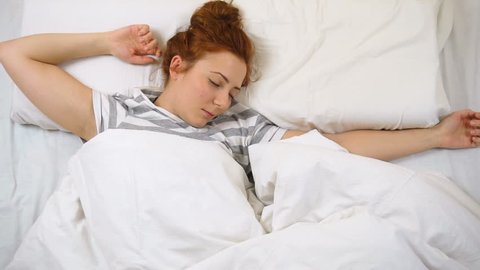 Foxy girl in T-shirt sleeping in bed moving and smiling in her sleep