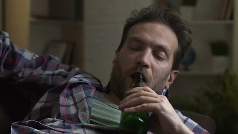 Guy drinking beer from bottle and falling asleep sofa, alcoholism and bad habits