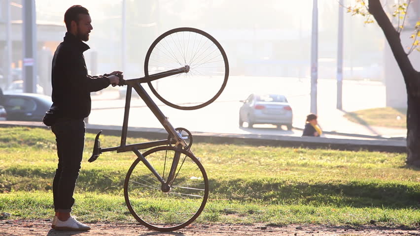 Handsome man preparing for the ride his bicycle in the park at sunset