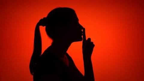 Silhouette of woman on red background. Female's face in profile putting finger to lips making silence gesture. Black contur shadow of teenager's half-face shushing. Concept of mystery and secrecy